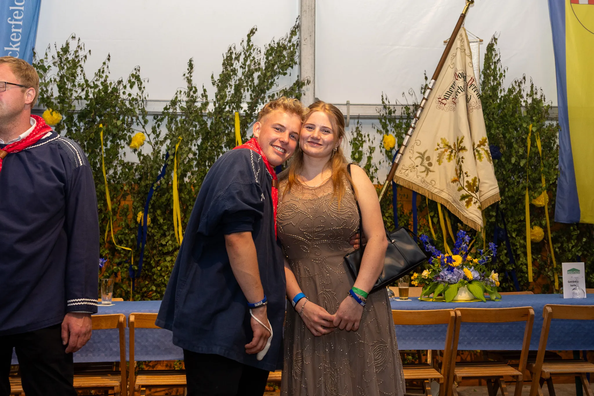 Ein Paar umarmt sich auf dem Königsball der Bauernschützen im Festzelt. Im Hintergrund ist eine Banner zu sehen und Tische mit Dekorationen.