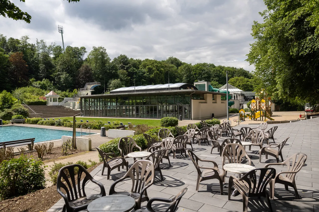 Freiluftbad Nattenberg mit Schwimmbecken, Liegewiese, Restaurantbereich mit Tischen und Stühlen sowie Kinderspielplatz.
