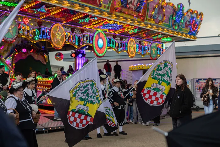 Trachtengruppe mit Fahnen vor bunt beleuchtetem Karussell während der Eröffnung der Halveraner Kirmes.