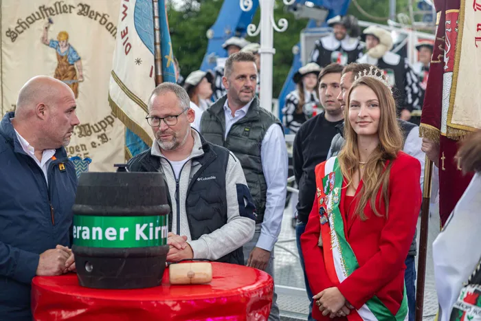 Bürgermeister Armin Kibbert schlägt ein Bierfass bei der Eröffnung der Halveraner Kirmes an, eine junge Frau in Tracht lächelt daneben.