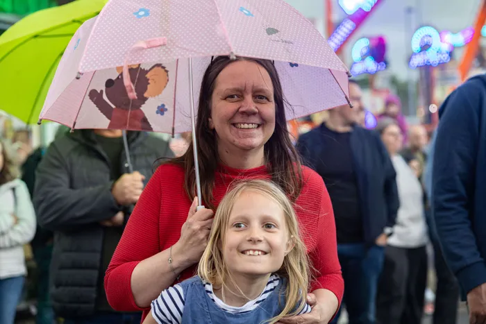Lachende Frau mit blondem Mädchen unter einem rosa Schirm mit Tiermotiven auf der Kirmes.