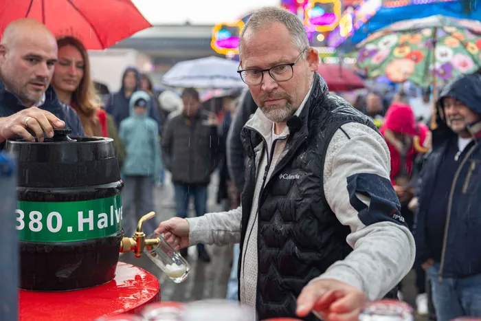 Bürgermeister Armin Kibbert zapft bei der Eröffnung der 380. Halveraner Kirmes ein Bierfass an, umgeben von Besuchern und bunten Lichtern des Festes.