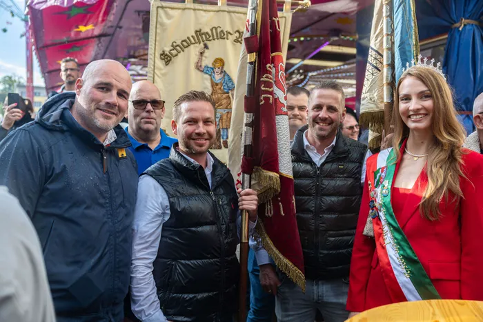 Bürgermeister Armin Kibbert hält eine Kirmesfahne, umgeben von weiteren Männern und einer Frau mit Krone und Schärpe bei der Eröffnung der Halveraner Kirmes.