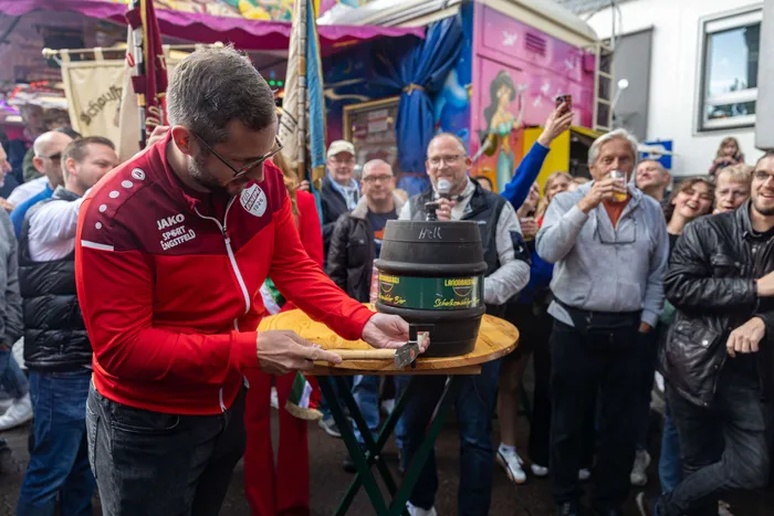 Bürgermeister Armin Kibbert sticht ein Bierfass an, um die 380. Halveraner Kirmes zu eröffnen, umgeben von Zuschauern.
