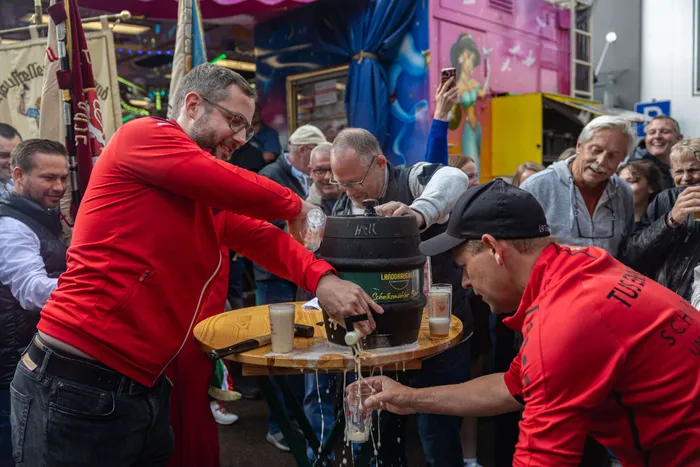 Bürgermeister Armin Kibbert zapft ein Bierfass auf der Halveraner Kirmes an, während ein Mitarbeiter ihm hilft und im Hintergrund Menschen zusehen.