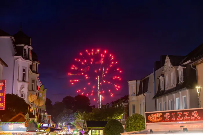 Rotes Feuerwerk erhellt den Nachthimmel über der belebten Kirmes in Halver.