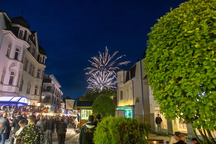 Feuerwerk erhellt den Nachthimmel über der belebten Kirmes in Halver, umgeben von Gebäuden und Bäumen.