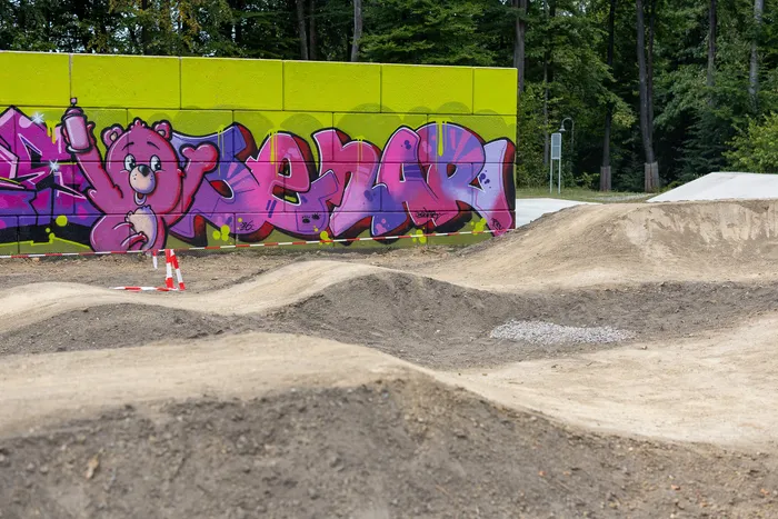 Erdhügel und Fahrspuren vor einer hellgrünen Wand mit buntem Graffiti im Bikepark Halver.