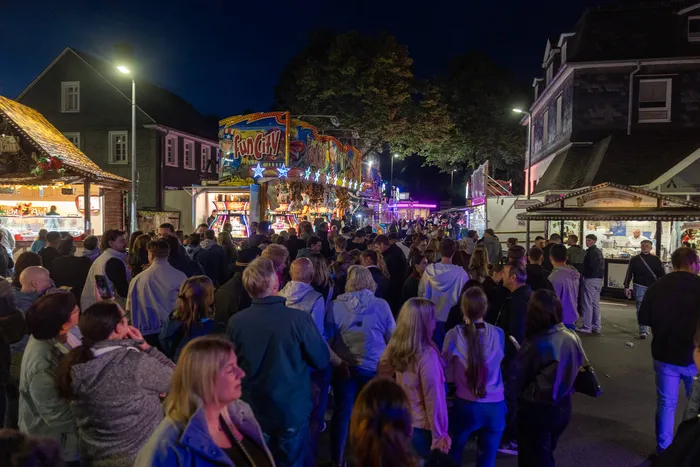 Menschenmassen auf der beleuchteten Kirmes, im Hintergrund ein beleuchteter Jahrmarktstand mit der Aufschrift „Fun City“.