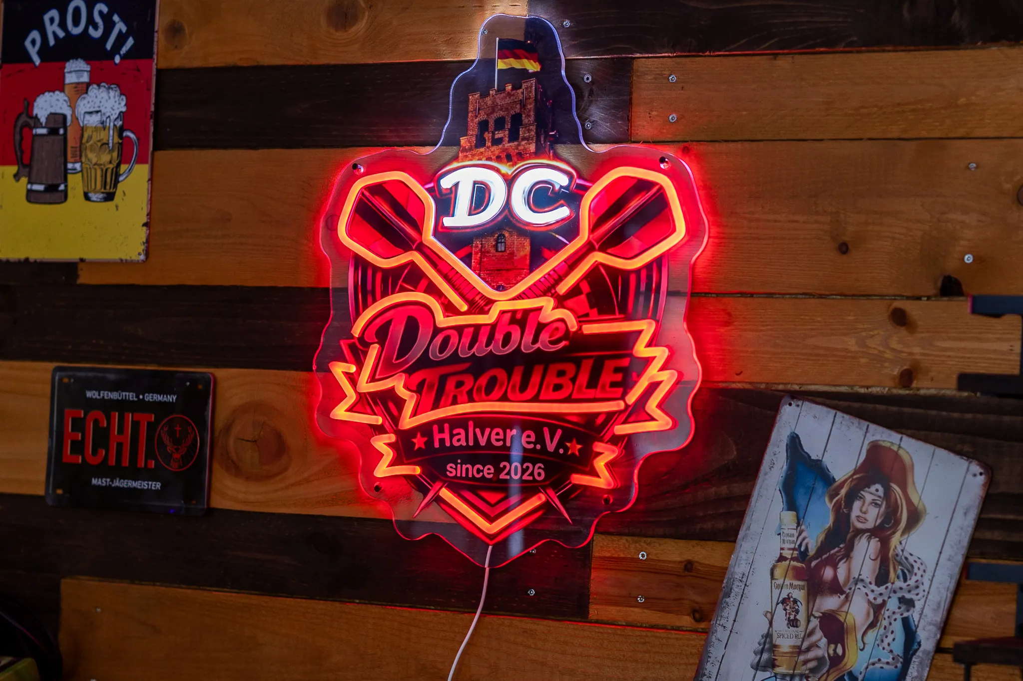 Leuchtendes Logo des Vereins „Double Trouble Halvere.V.“ mit stilisierter Burg und dem Schriftzug „since 2026“ an einer Holzwand.