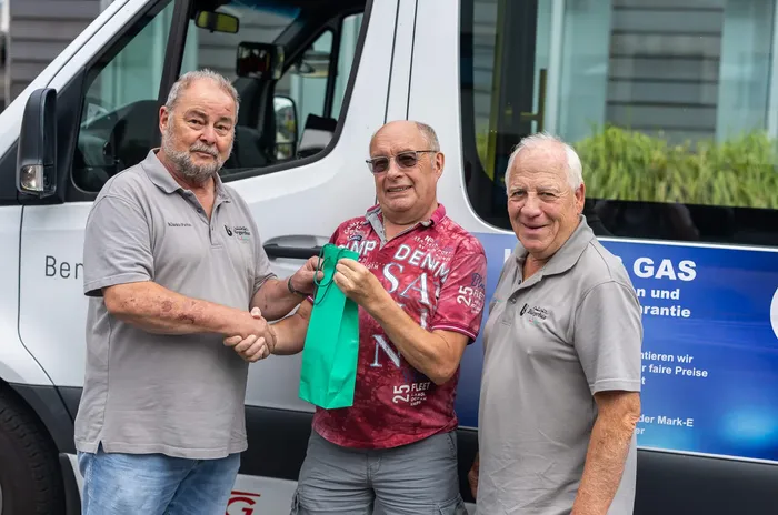 Klaus-Peter Viebahn schüttelt Peter Baumgart die Hand, während Horst Rzonsa daneben steht. Die drei Männer stehen vor einem weißen Transporter.