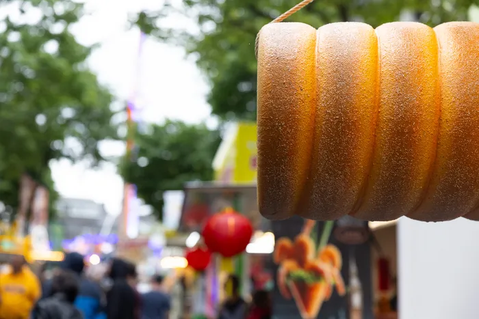 Nahaufnahme von mehreren in Zucker getauchten Halveraner Kirmesbrötchen, im Hintergrund Menschen und Buden auf der Kirmes.