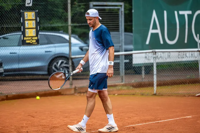 Ein Tennisspieler in weiß-blauem Outfit geht mit einem Schläger über einen Sandplatz bei den Halver Open.