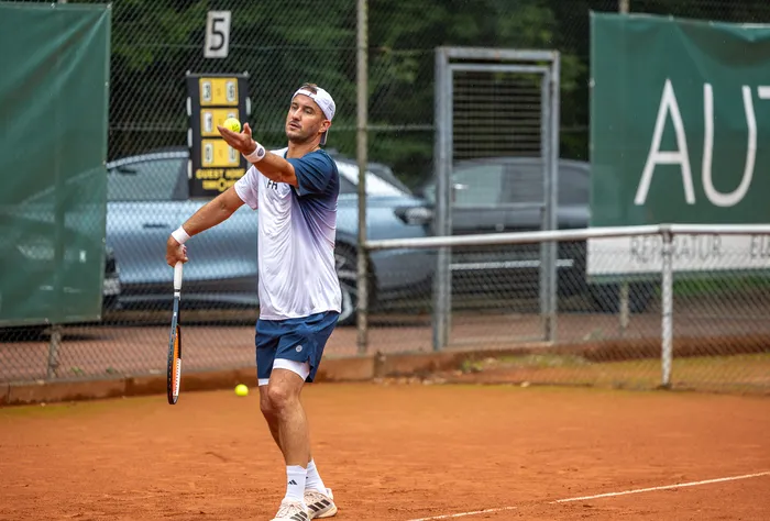Ein Tennisspieler bereitet einen Aufschlag auf einem Sandplatz vor, indem er den Ball in die Luft wirft.