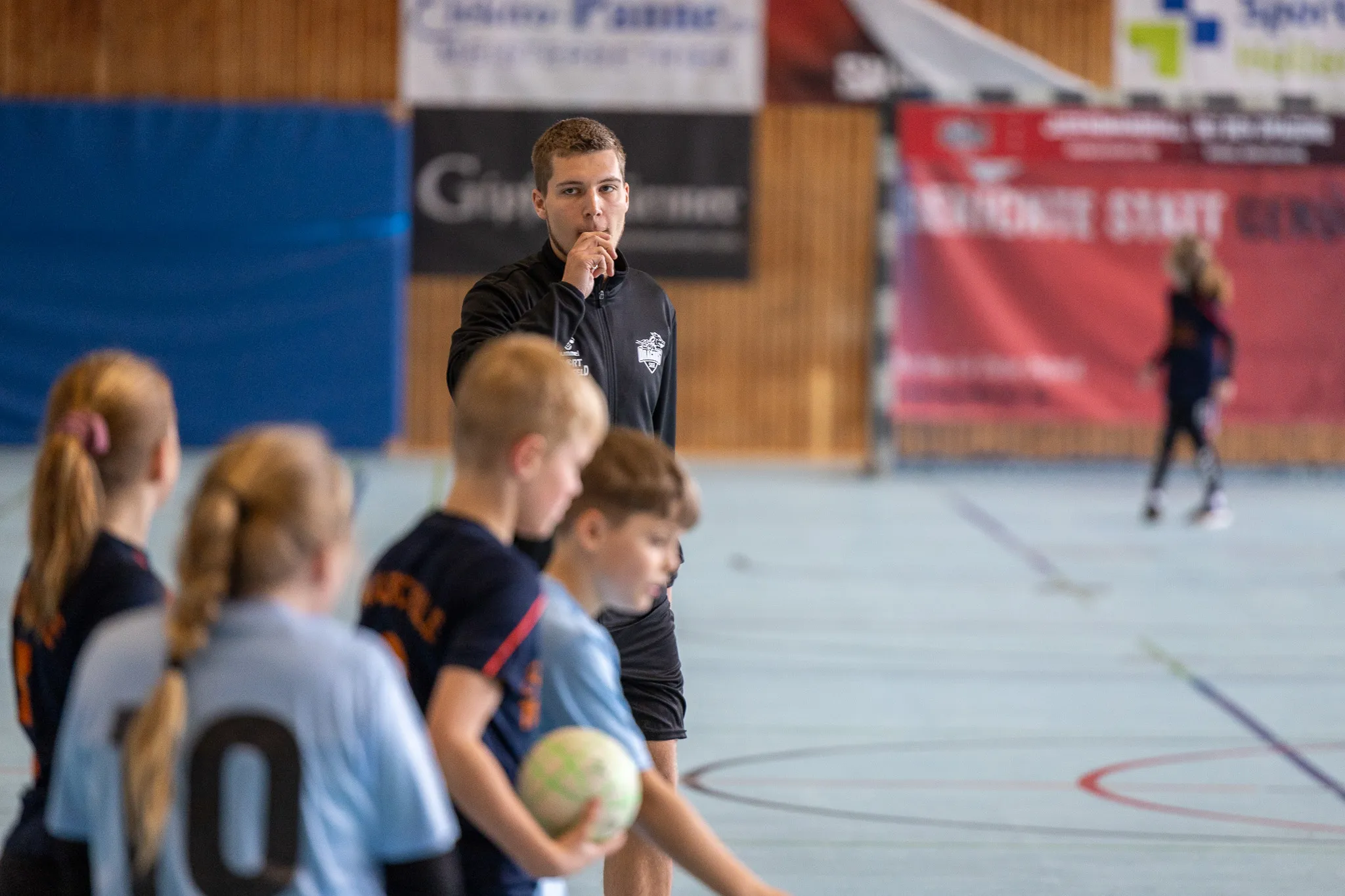 Trainer gestikulierend vor Jugendhandballmannschaft in Sporthalle während Kreismeisterschaften.