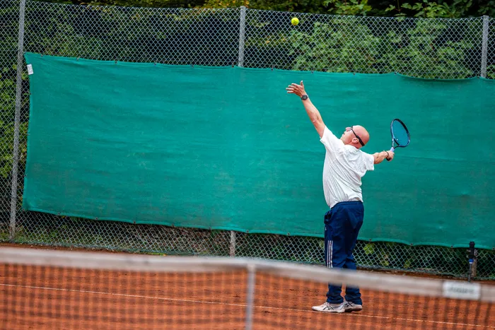 Ein Mann in weißem T-Shirt und blauer Hose schlägt bei der Halver Open auf einem Sandplatz einen Tennisball.