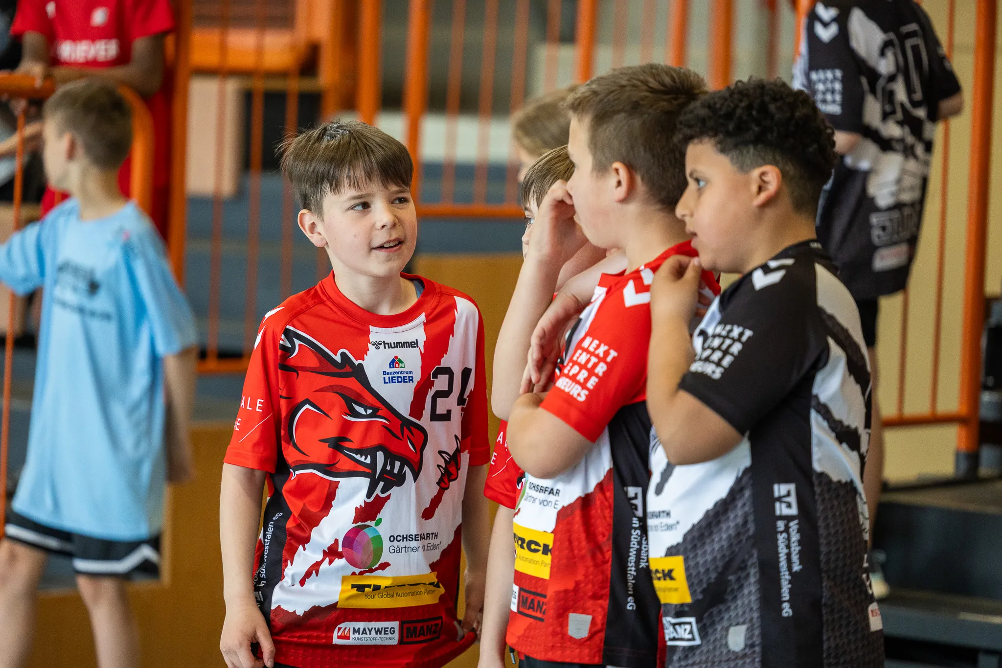 Jungenmannschaft im Handballtraining, einige Spieler stehen im Kreis und besprechen Taktiken, während andere im Hintergrund stehen.
