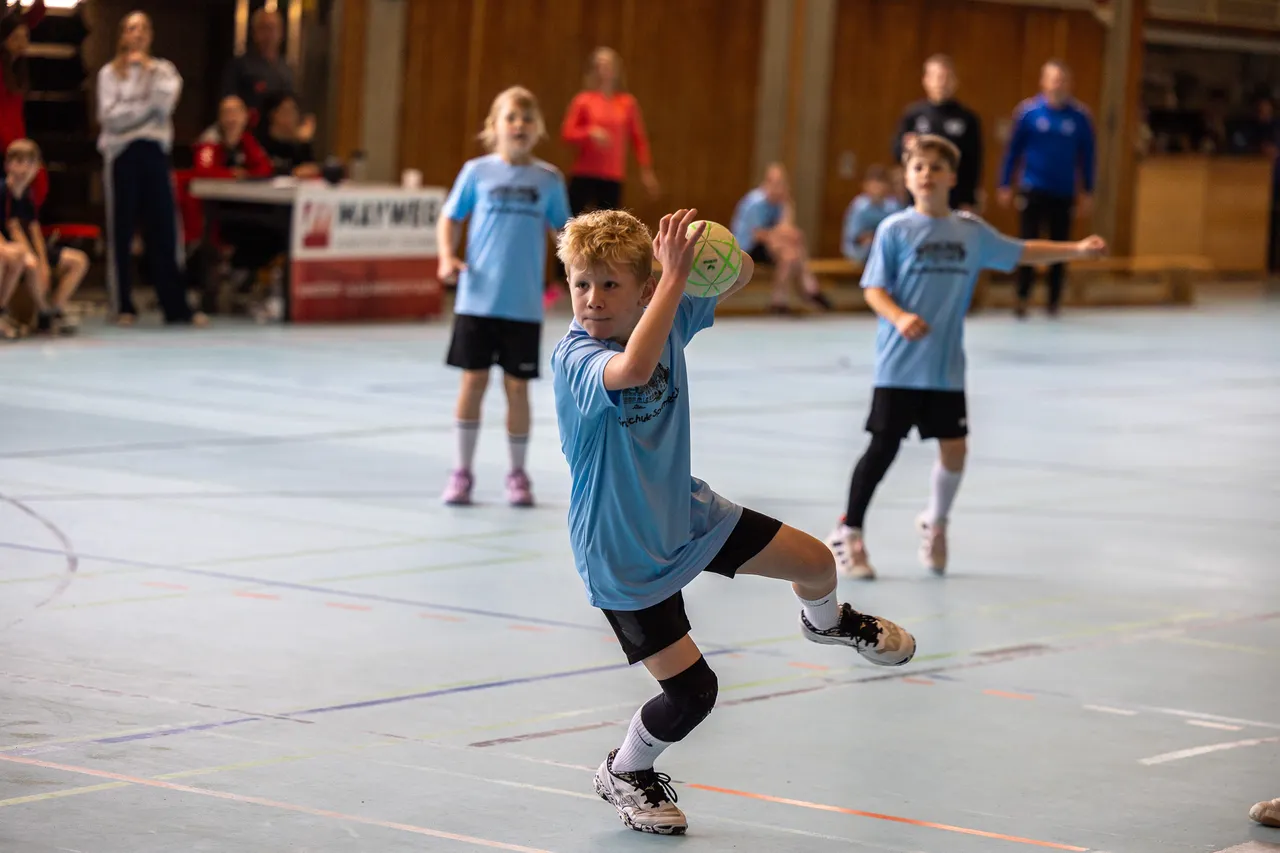 Ein Junge wirft im Hallensport einen Handball, während andere Kinder im Hintergrund stehen und zusehen.