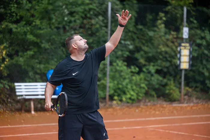 Ein Mann in schwarzer Sportkleidung bereitet einen Aufschlag auf einem Sandplatz vor.
