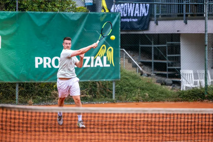 Ein Tennisspieler schlägt einen gelben Ball auf einem Sandplatz vor einem grünen Banner mit der Aufschrift „PROZIAL“.