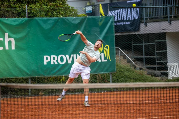 Ein Tennisspieler in weißer Sportkleidung schwingt seinen Schläger bei einem Schlag auf einem Sandplatz.