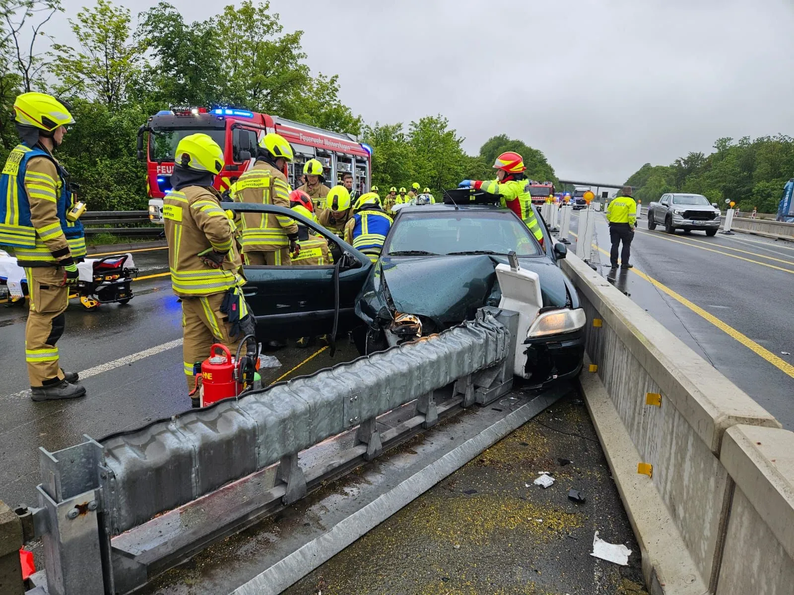 Ein stark beschädigtes Auto steht nach einem Unfall auf der Autobahn. Feuerwehrleute sind um das Wrack versammelt und leisten offenbar Erste Hilfe.