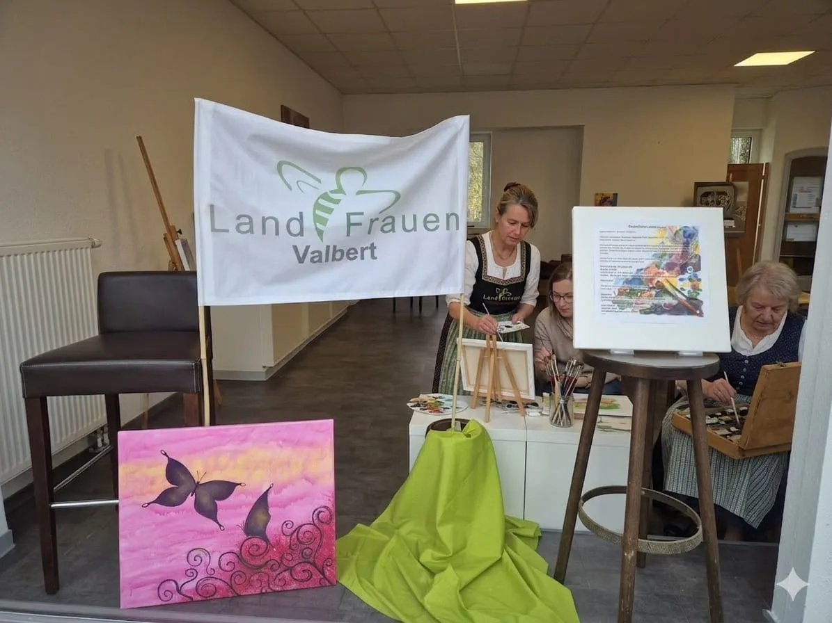 Drei Frauen malen in einem hellen Raum. Im Hintergrund ein Banner mit der Aufschrift „Landfrauen Valbert“.