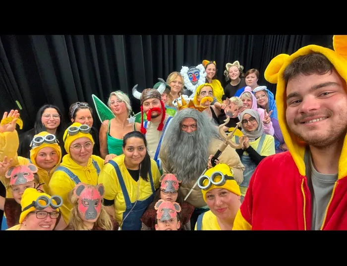 Eine Gruppe von Menschen in Kostümen, darunter Minions und ein Mann mit langem grauem Bart, posiert für ein Selfie. Im Vordergrund ein junger Mann in einem gelben Tierkostüm.