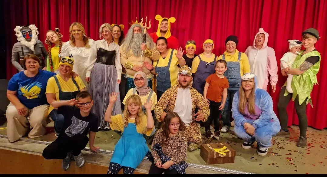 Die Kinder der AWO-Kita Wundertüte und ihre Unterstützer posieren nach der Aufführung des Theaterstücks „Die besondere Reise durch die Wundertüte“ in Kostümen auf der Bühne. Einige tragen Tierkostüme, andere sind als Figuren verkleidet.
