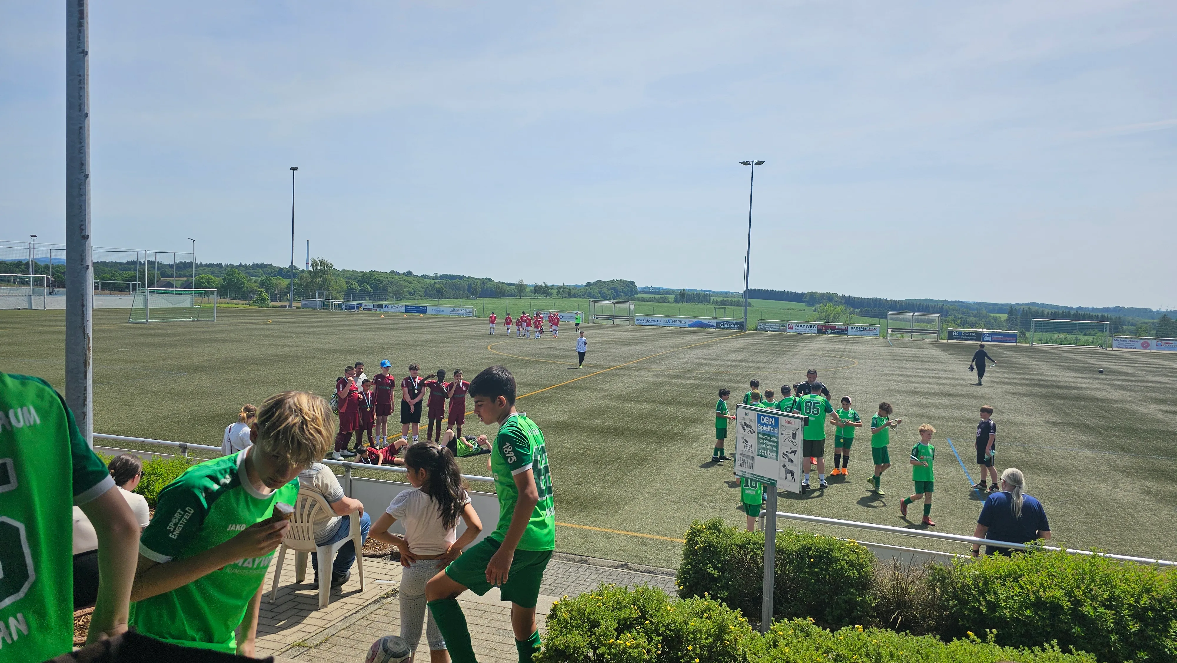 Fußballturnier mit Kindern und Jugendlichen auf einem Kunstrasenplatz, umgeben von Zuschauern und vereinseigenen Bannern.