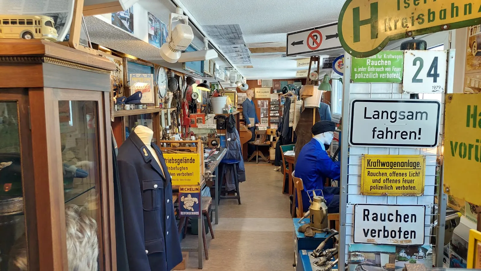 Innenansicht eines Museums mit Vitrinen voller Modellautos und historischer Verkehrsschilder. Ein Mann in blauem Overall steht im Hintergrund und betrachtet die Ausstellungsstücke.