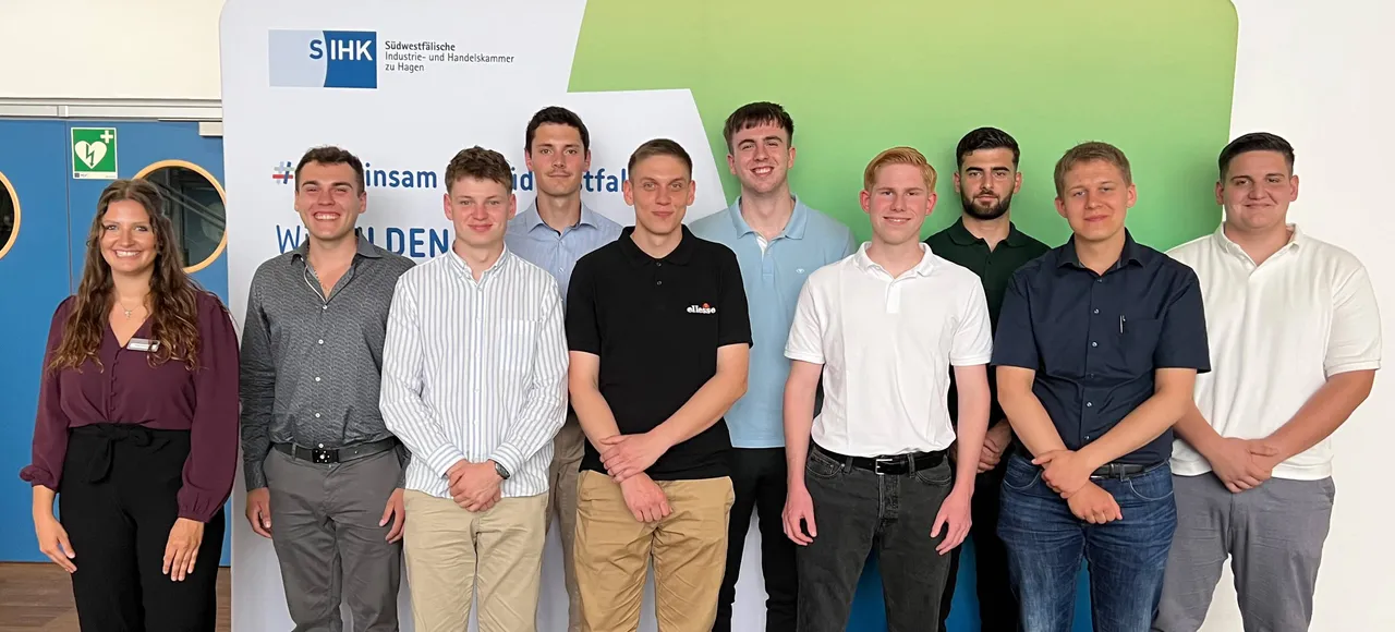Gruppe von zehn jungen Berufstätigen und einer Projektkoordinatorin der SIHK vor einem Banner mit dem Aufdruck „insam id tfall“ und dem Logo der Südwestfälischen Industrie- und Handelskammer.