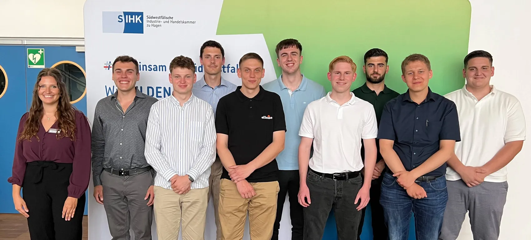 Gruppe von zehn jungen Berufstätigen und einer Projektkoordinatorin der SIHK vor einem Banner mit dem Aufdruck „insam id tfall“ und dem Logo der Südwestfälischen Industrie- und Handelskammer.