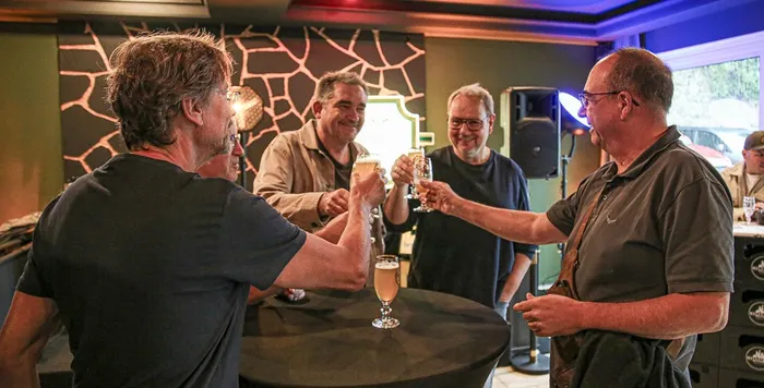 Eine Gruppe von Männern stößt bei einer Feier mit Gläsern voll Pilsner gemeinsam an.