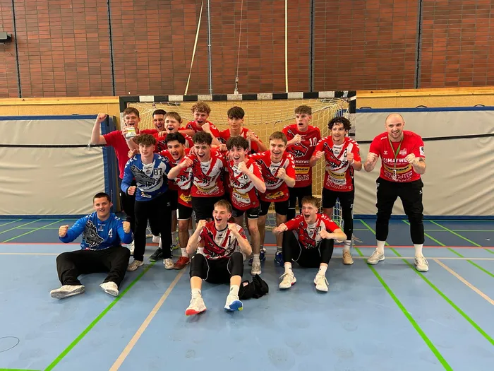 Mannschaftsfoto der jubelnden A-Jugendhandballmannschaft SGSH in rot-schwarzen Trikots und Trainingsanzügen nach einem gewonnenen Spiel.