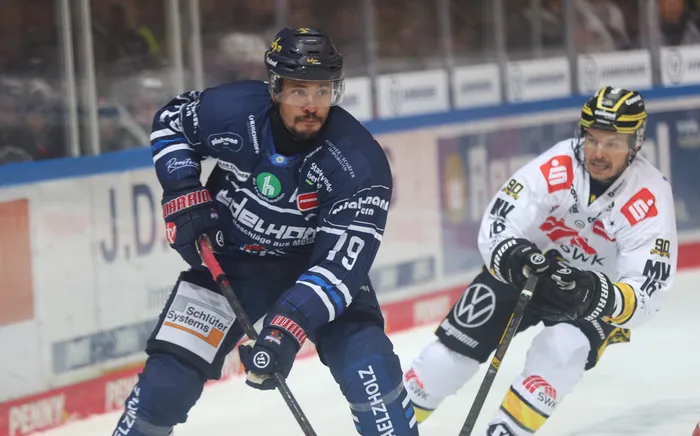 Zwei Eishockeyspieler in blauen und weißen Trikots während eines Spiels auf dem Eis.