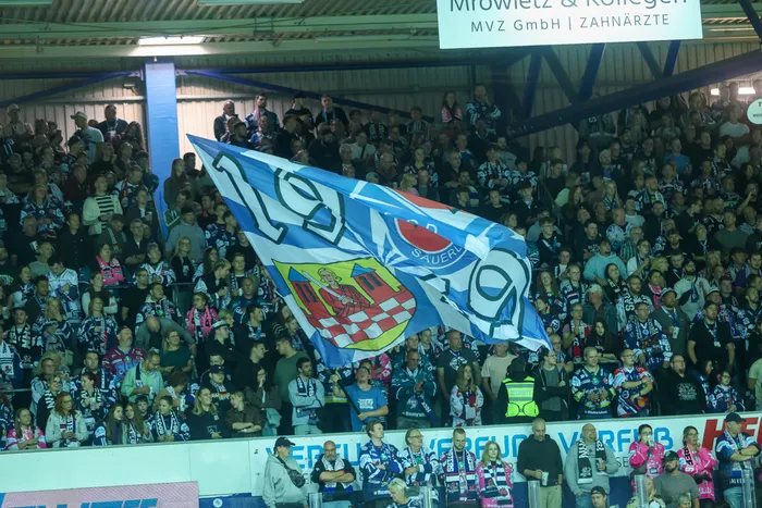 Eine große Menschenmenge in einem Stadion schwenkt eine große blau-weiße Flagge mit einem Wappen.