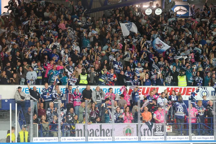 Jubelnde Fußballfans in blau-weißer Kleidung schwenken Fahnen in einem Stadion.