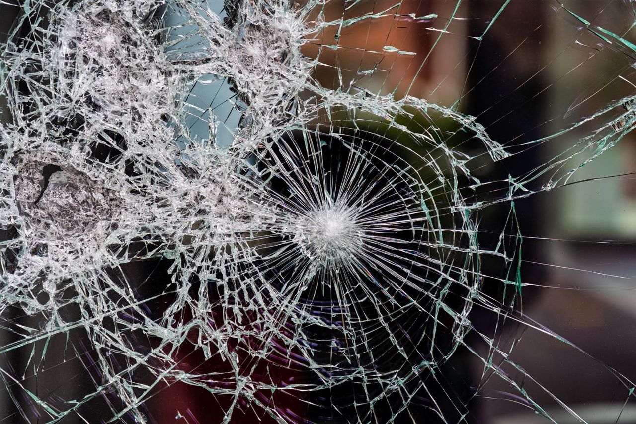 Nahaufnahme einer stark zersplitterten Glasscheibe mit einem zentralen Einschlagspunkt.