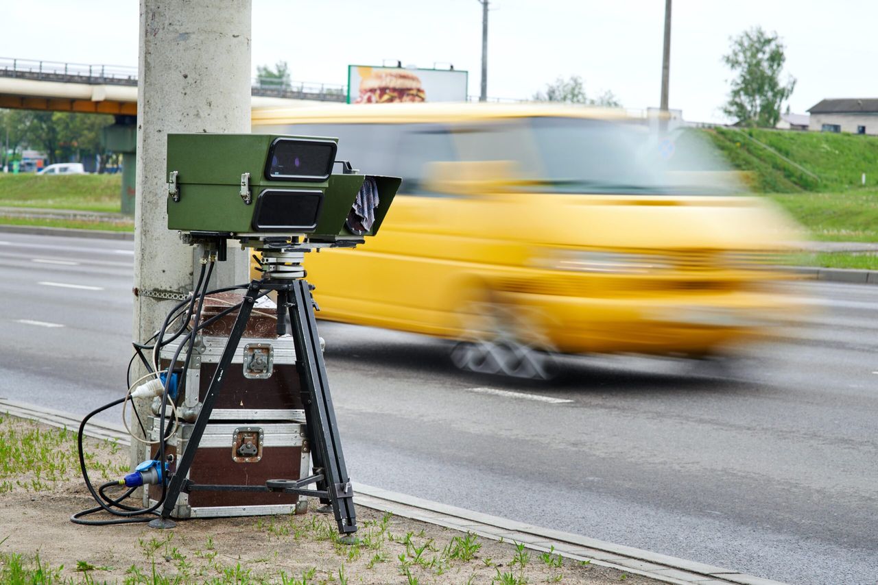 Ein mobiler Blitzer steht am Straßenrand, während ein gelber Bus mit hoher Geschwindigkeit vorbeifährt.