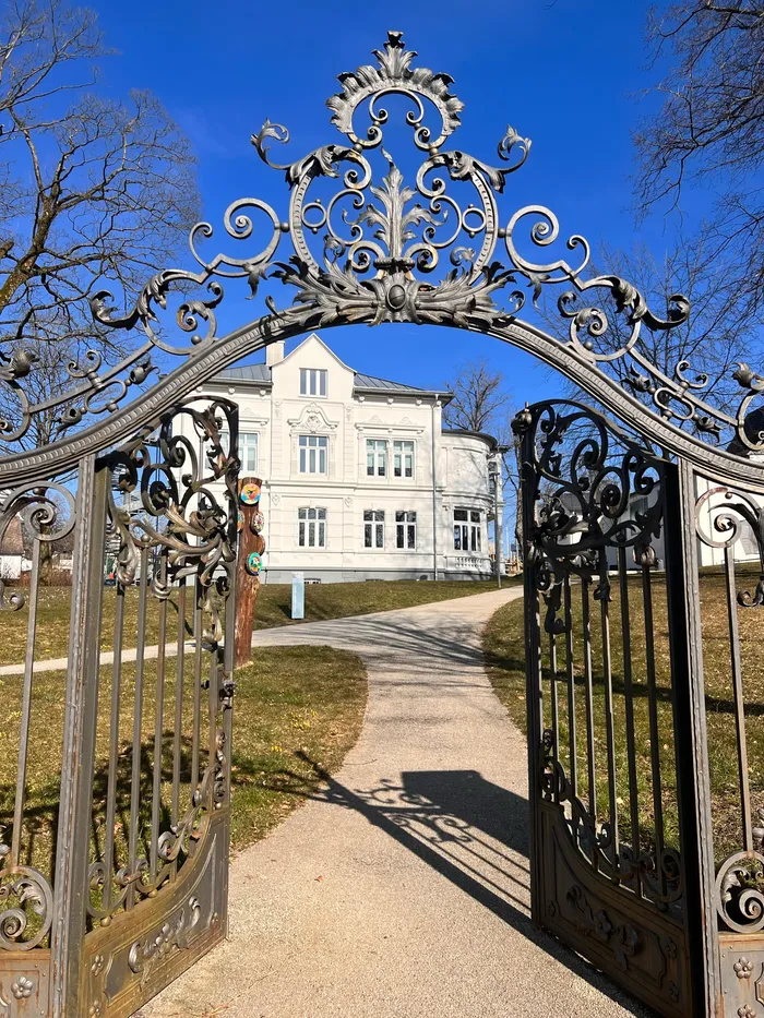 Eiserne Eingangstore öffnen den Blick auf die helle Villa Wippermann mit symmetrischer Fassade und mehreren Fenstern.