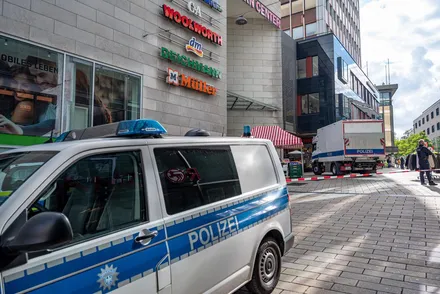 Polizeifahrzeuge blockieren eine Straße vor einem Einkaufszentrum mit Geschäften wie Woolworth, DM und Deichmann.