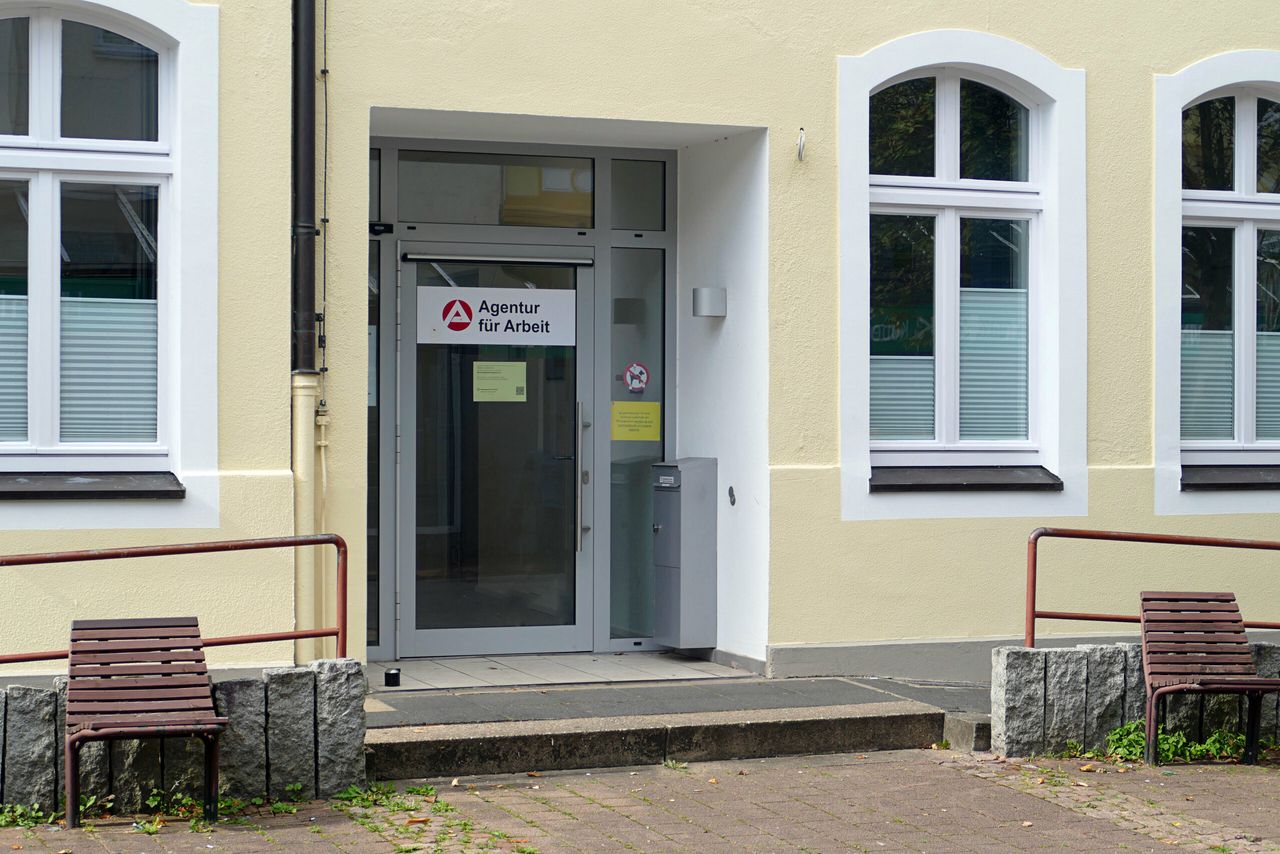 Agentur für Arbeit in Werdohl, Fassade mit Eingangsbereich und zwei Bänken davor. Das Gebäude ist hellgelb und hat große Fenster.
