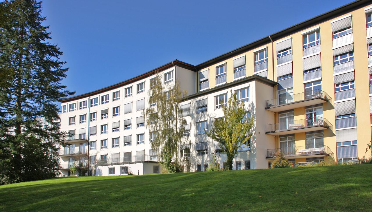 Gebäude des Radprax-Krankenhauses Plettenberg mit mehreren Stockwerken und Balkonen, umgeben von Grünflächen.