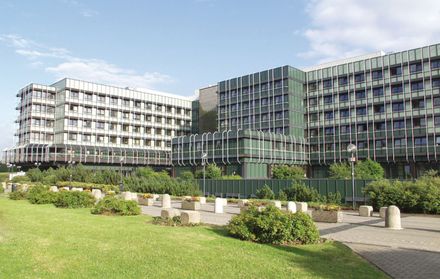 Das mehrstöckige Klinikum Lüdenscheid mit seiner Fassade aus vielen Fenstern steht inmitten einer Grünanlage mit gepflegten Beeten und Rasenflächen.