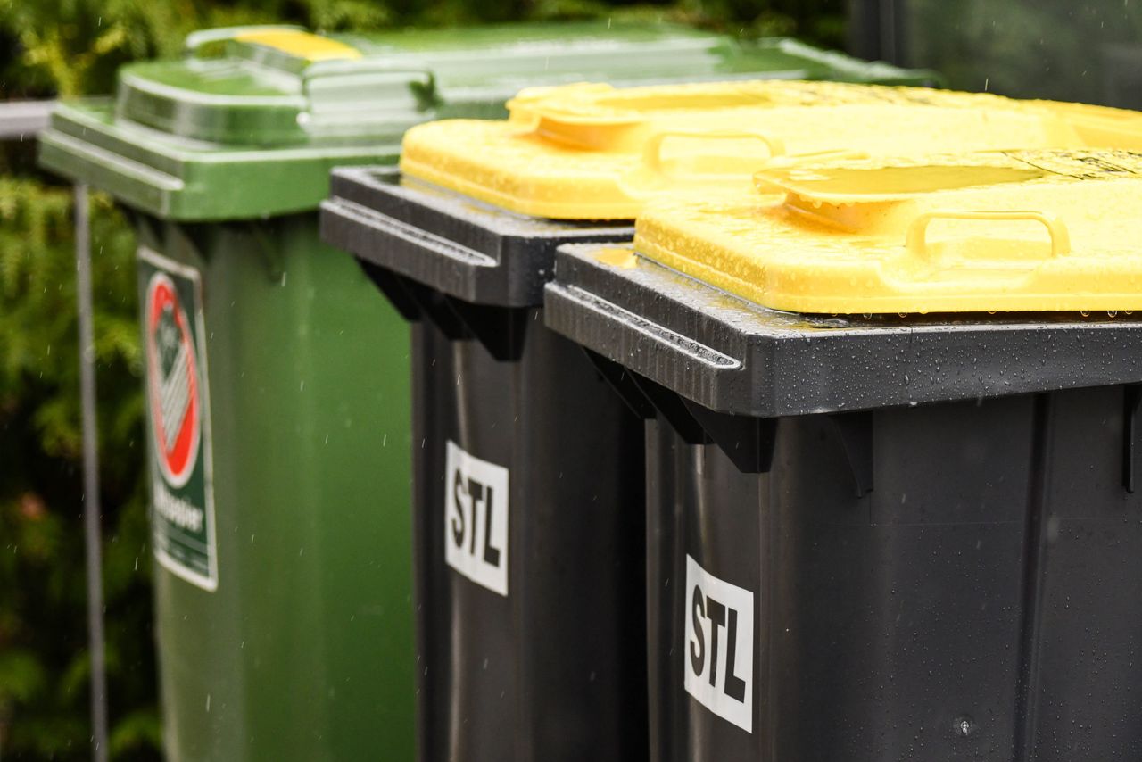 Grüne und gelbe Mülltonnen mit dem Aufdruck „STL“ stehen im Regen.