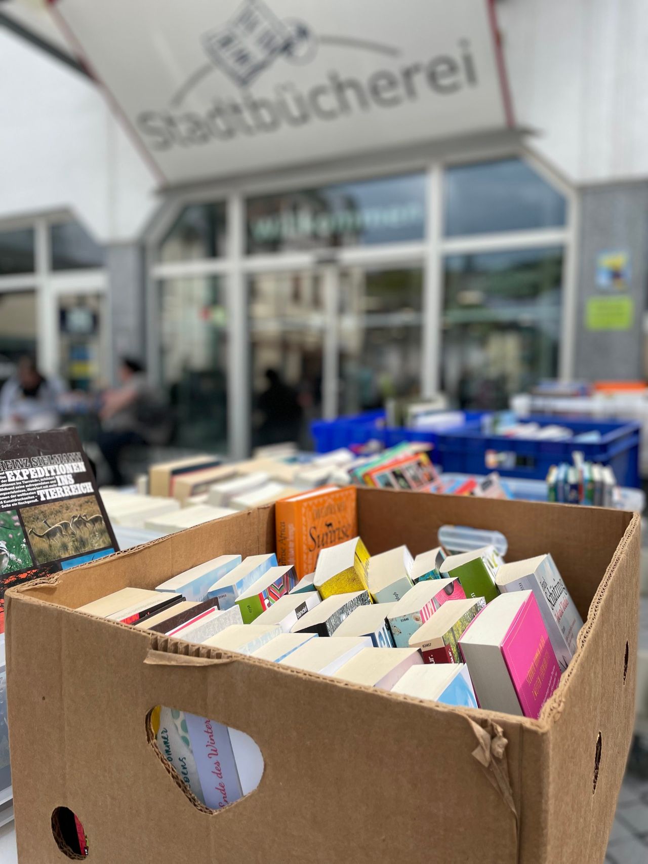 Eine Pappschachtel voller Bücher auf einem Bücherflohmarkt vor der Stadtbücherei.