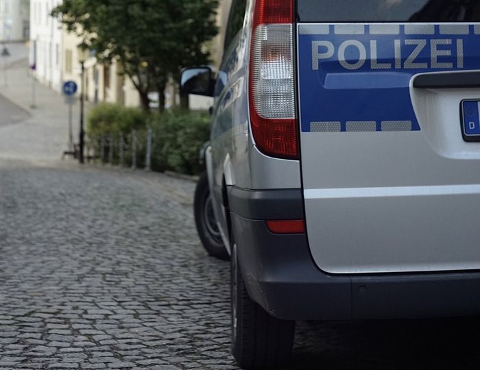 Heckansicht eines Polizeiwagens mit der Aufschrift „POLIZEI“ auf einer Kopfsteinpflasterstraße.