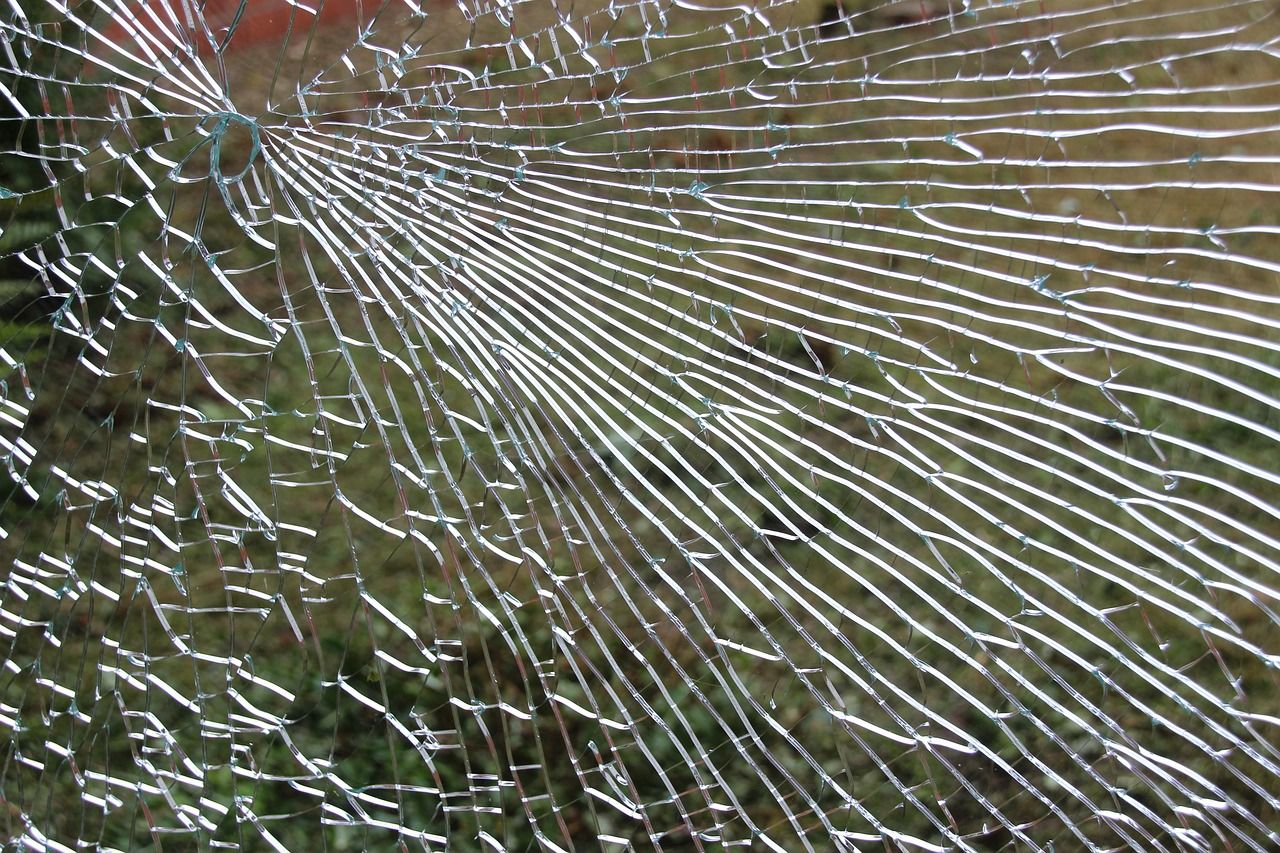 Zersplitterte Glasscheibe mit sternförmigem Bruchmuster vor unscharfem Hintergrund.