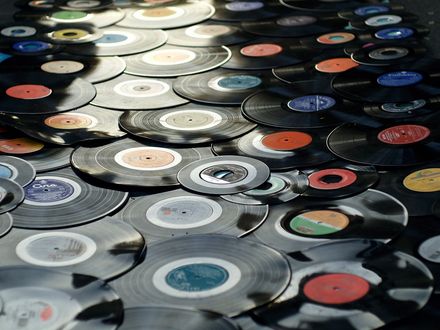 Viele gebrauchter Schallplatten liegen dicht an dicht auf einer dunklen Oberfläche. Die farbigen Etiketten der Schallplatten sind unterschiedlich gestaltet.